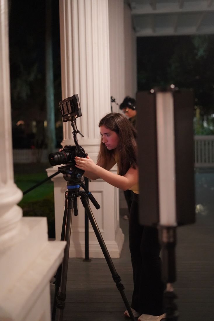 A crew member sets up the camera on a tripod on a porch at night