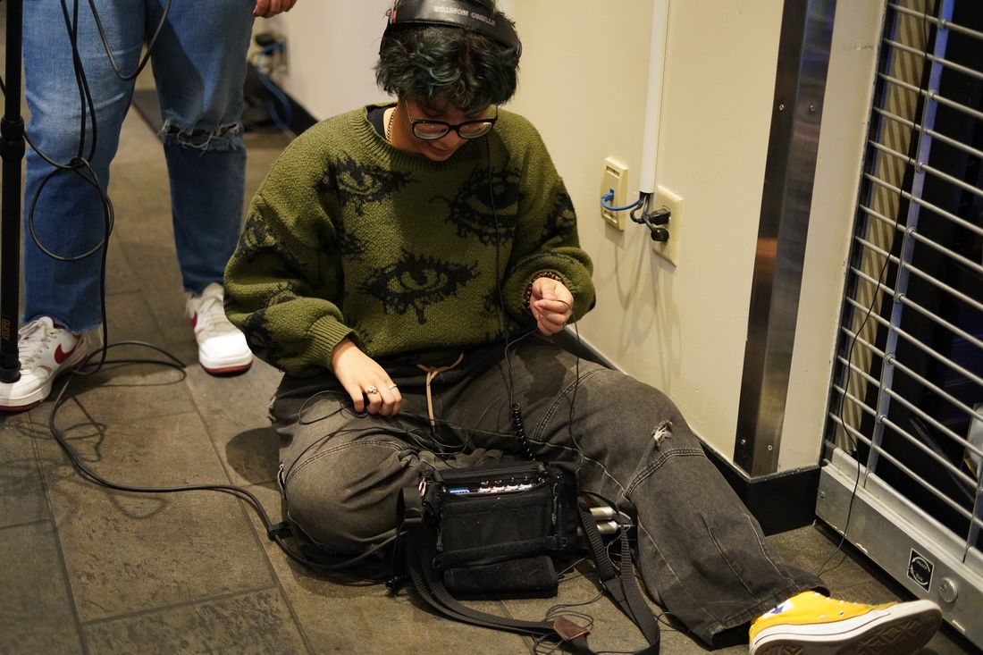 The sound recordist sits on the floor adjusting the audio mixer