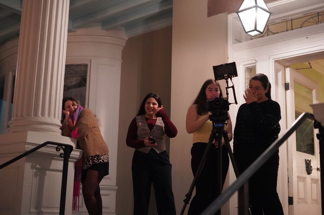 Crew members gather around the camera on a porch at night