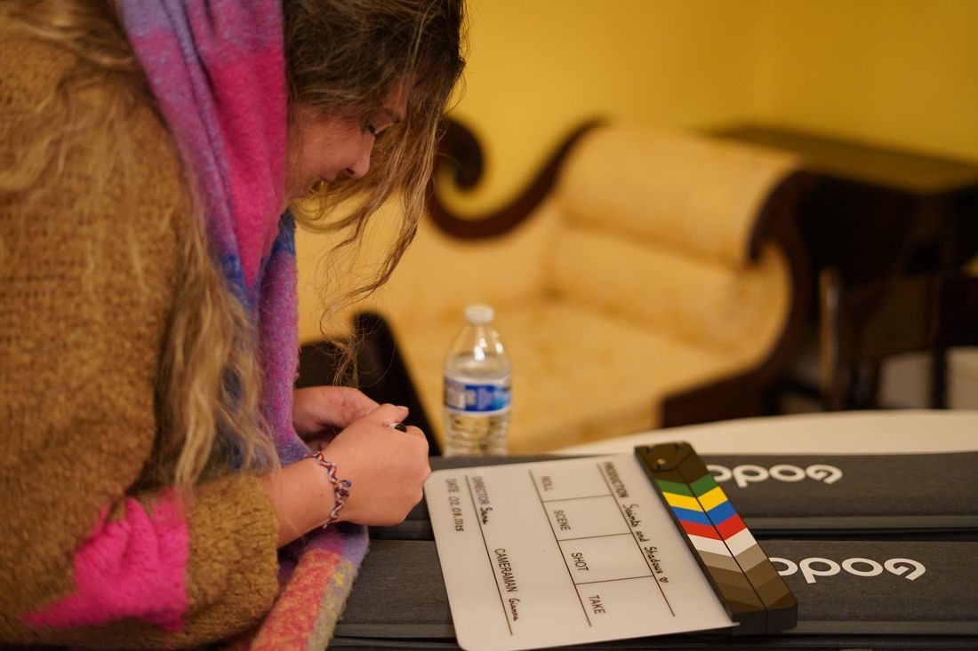 A crew member writes on the clapperboard, which reads Saints and Shadows
