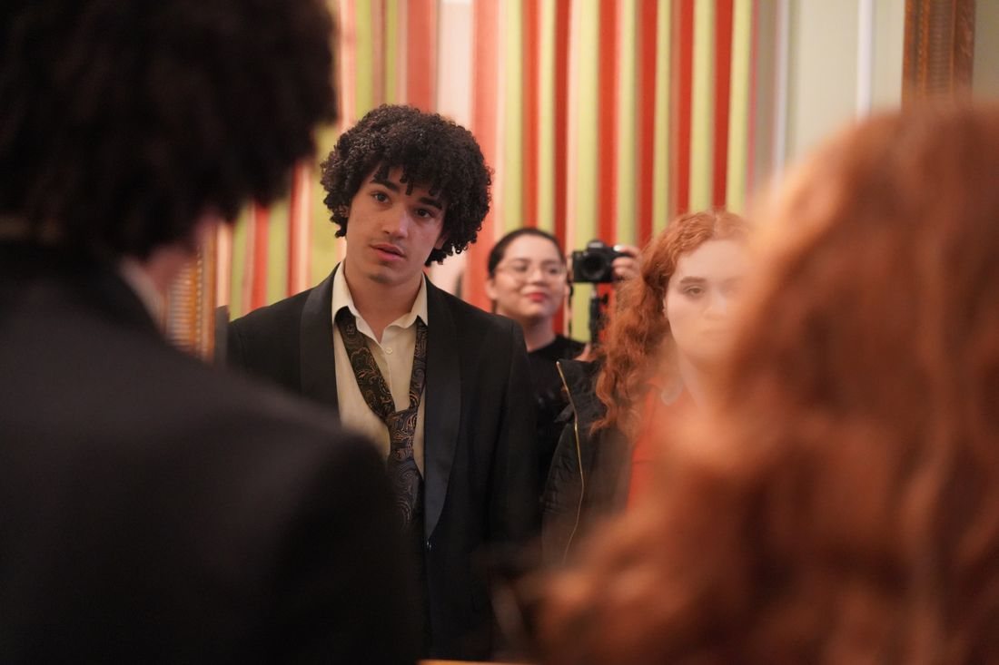 An actor in a suit during a take, with the camera visible behind him