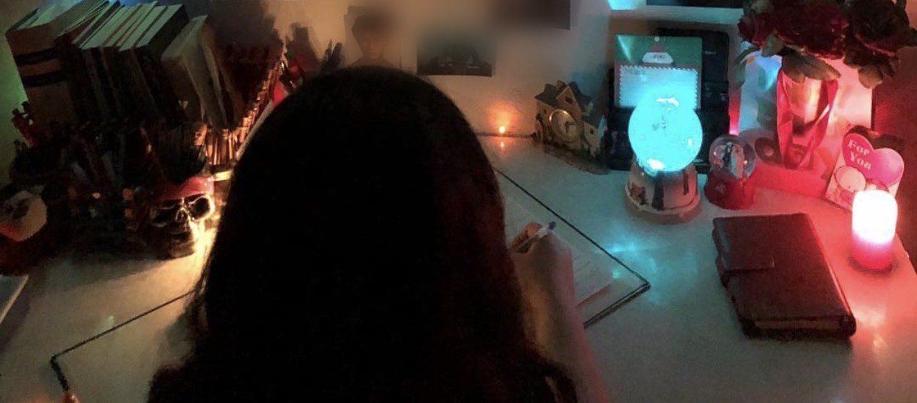 Sana Mohtasebzada seen from behind, writing by hand at her desk at night by the light of a candle and a lamp