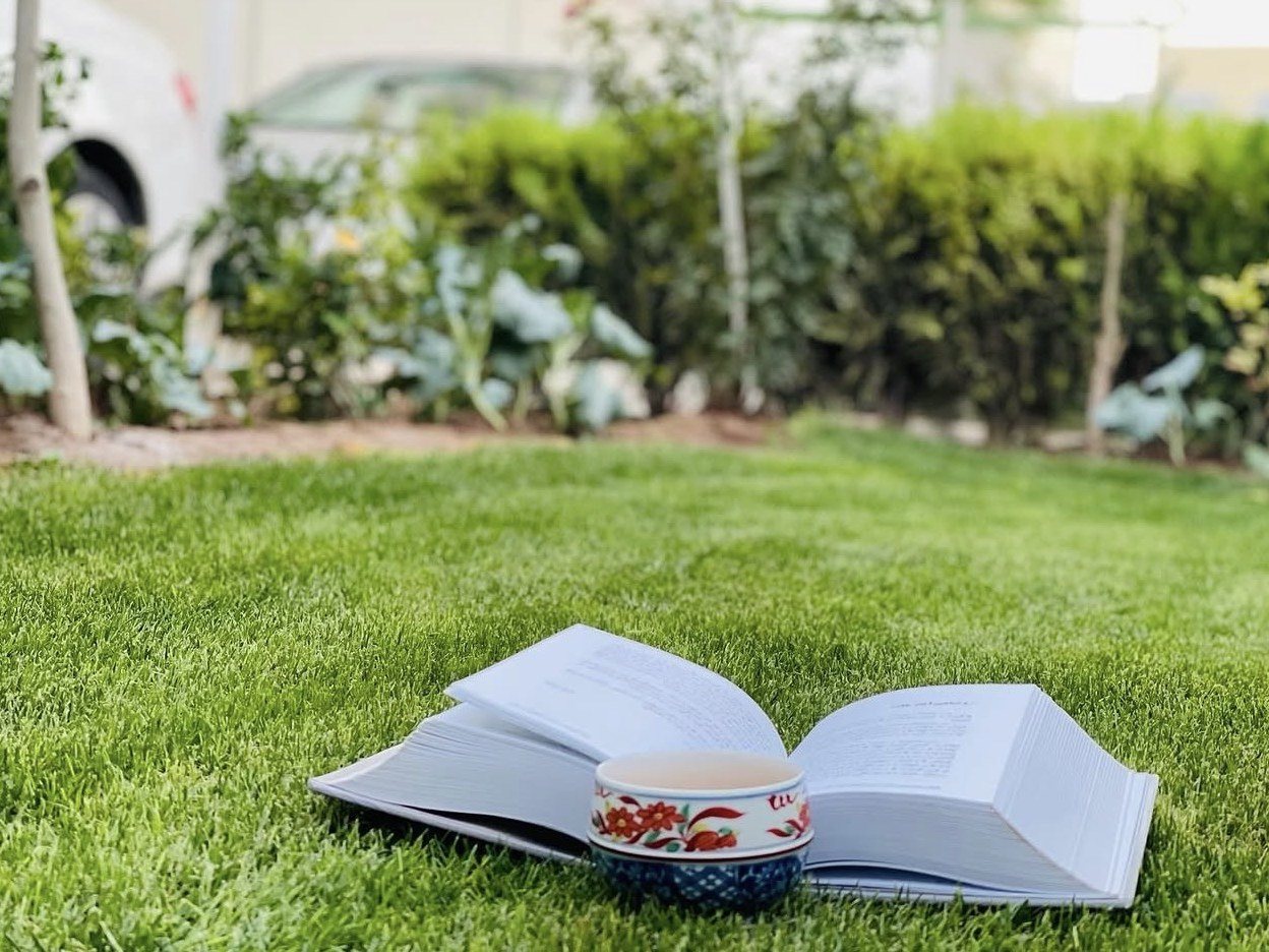 An open book and a cup of tea on the lawn of a garden