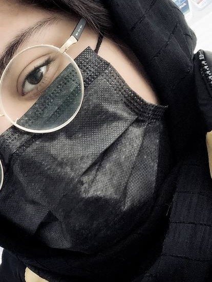 A close self-portrait of Sana Mohtasebzada with her face covered by a black mask and scarf, one eye visible behind round glasses