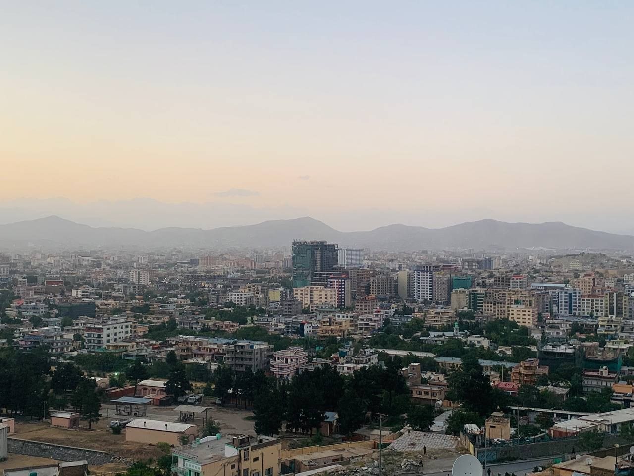 Kabul at dusk, seen from a hillside, with mountains behind the city