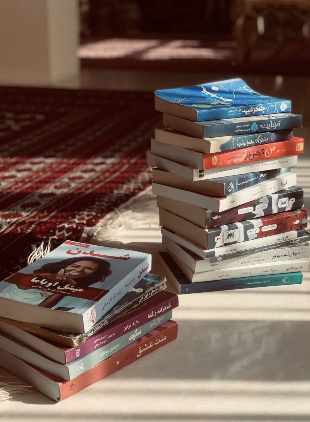 Two stacks of books on the floor in sunlight, beside a red carpet